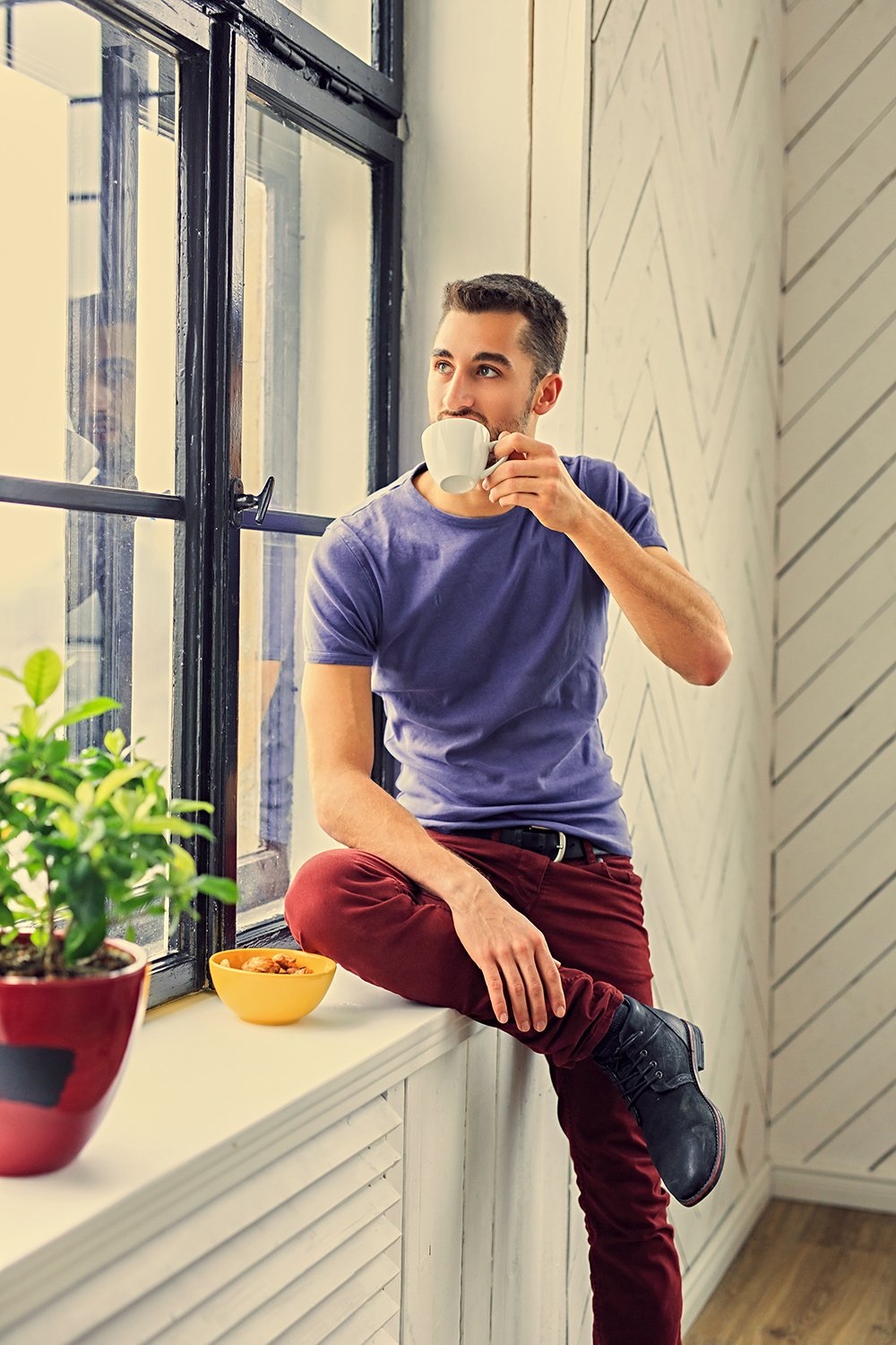 Casual young man drinks coffee near the window. Filtered warm toned image.