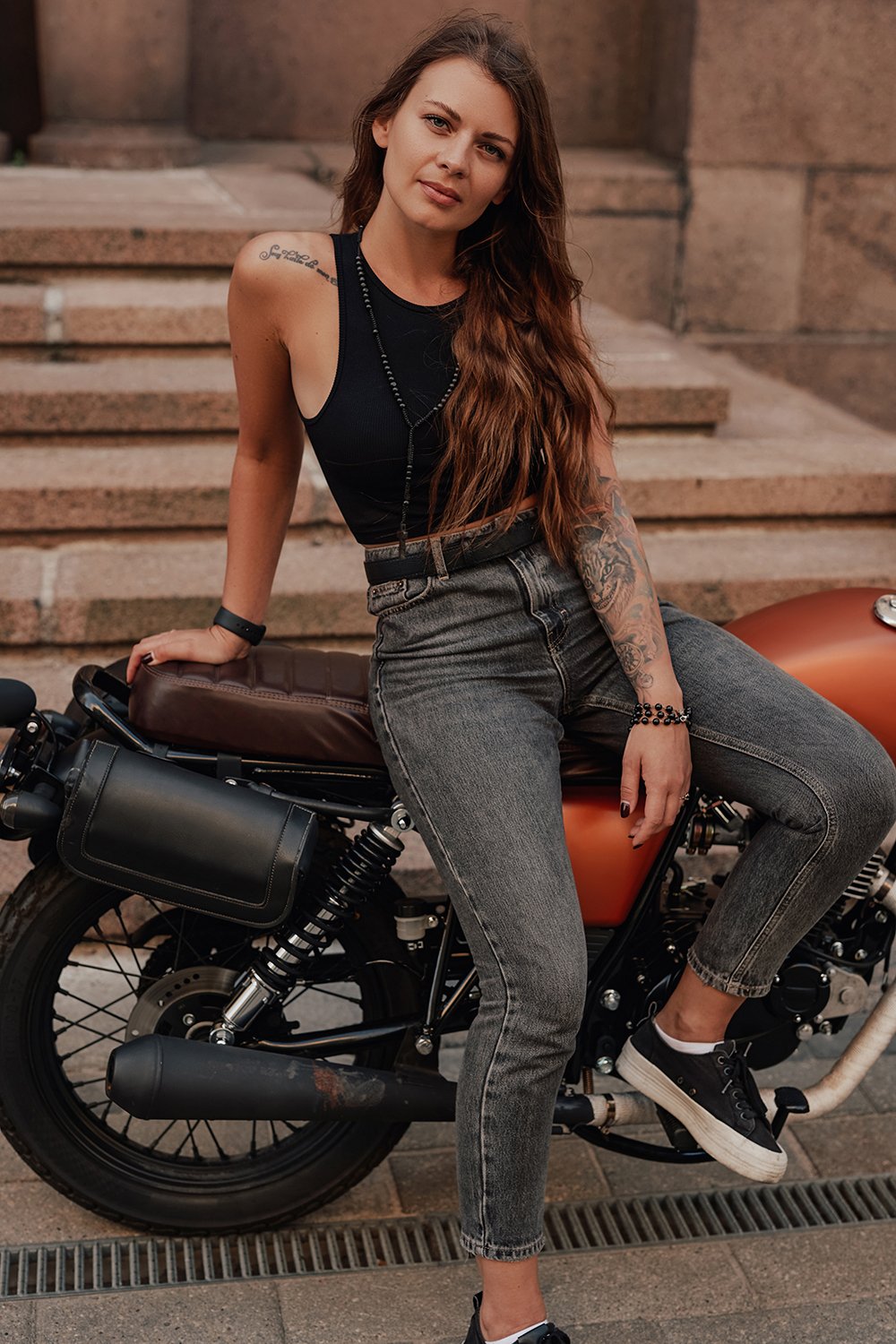 Shot of woman motorcyclist dressed in stylish summer clothes posing on retro style bike in town.