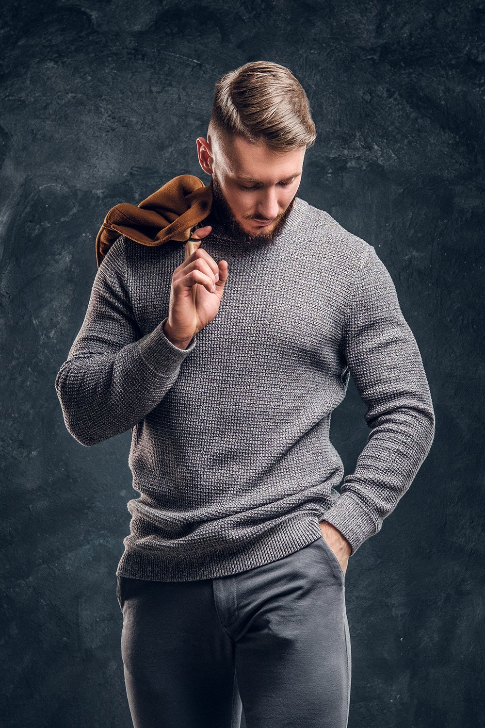 Men's beauty, seasonal fashion. Portrait of a stylish male holding his demi-season coat. Studio photo against dark wall background